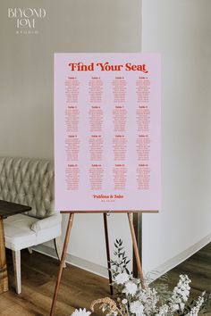 a seating chart is displayed on an easel in front of a couch and flowers