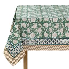 a green table cloth with white flowers and leaves on the border, sitting on top of a wooden table