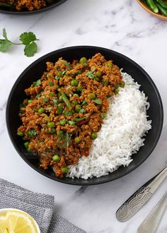 a bowl filled with rice and meat next to a spoon, lemon wedges and cilantro