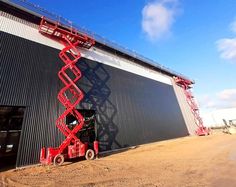 a red scissor sits in front of a large building with a sky background