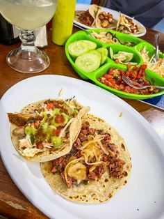 three tacos are sitting on a white plate next to some pickles and cucumbers