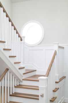 a white staircase with wooden handrails and a round window above the banister