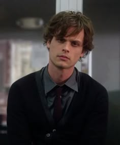 the young man is wearing a black sweater and tie with his hands on his chest