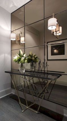 a glass table with vases and flowers on it in front of a mirror wall