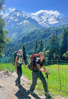 two people with backpacks are walking up a trail in the mountains near a fence