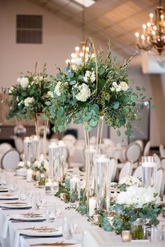 there are many tall vases with flowers on the long table at this wedding reception