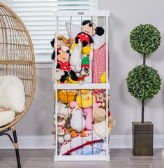 a shelf filled with lots of stuffed animals next to a chair and potted plant