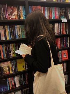 a woman standing in front of a bookshelf holding a book and looking at it