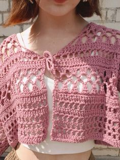 a woman is wearing a pink crocheted sweater with an openwork design on it