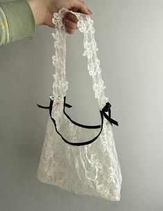 a hand holding a white lace bag with black ribbon around the strap and an embellished smile on it