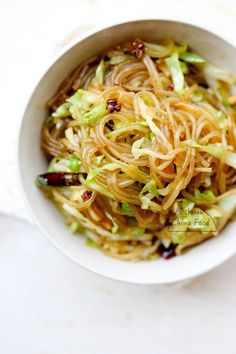 a bowl filled with noodles and vegetables on top of a white table cloth next to a fork