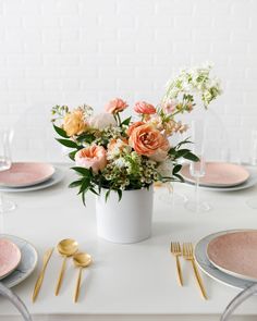 an arrangement of flowers in a white vase on a table with pink plates and goldware