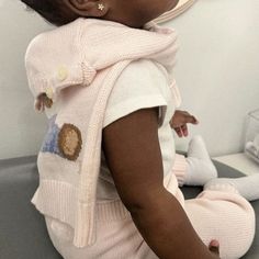 a baby wearing a pink sweater and white pants sitting on top of a table next to a stuffed animal