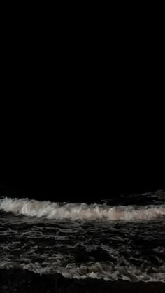 a man standing on top of a surfboard next to the ocean in the dark