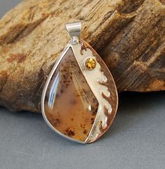 This pendant features a wonderful Montana Agate cabochon. It is a creamy golden color, with dark dendritic patterns inside. I love the elegant shape Juvy Andres of JC Cabochons gave it. I set the stone in a fine silver bezel on a sterling silver back and added a hammered copper dendritic border along one side. I darkened the copper and polished it to bring out the texture, and to compliment the stone. A little 4mm Golden Citrine brings out the gold of the agate. The bail is riveted. Don't forget that Citrine is one of November's birthstones! SIZE: The pendant measures about 1 3/4 inches long and 1 1/8 inch wide. This pendant is sold without a chain (please select 0 inches) or with a sterling silver chain in the length of your choice. PROPERTIES OF STONES (information compiled from numerous Metalworking Jewelry, Agate Necklaces, Bronze Bangle, Glass Fusing Projects, Metalsmithing Jewelry, Soldering Jewelry