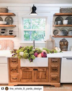 a kitchen with wooden cabinets and open shelves on the wall, filled with fresh vegetables