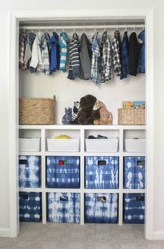 an organized closet with blue and white boxes, baskets and clothes hanging on the wall