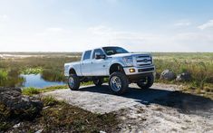 a white truck parked on the side of a dirt road next to a body of water