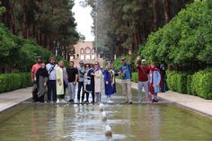 a group of people standing next to each other near a water fountain with trees in the background