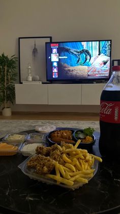 a table topped with plates of food next to a bottle of soda and a tv