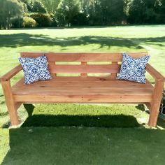 a wooden bench sitting on top of a green grass covered park field with two blue and white pillows