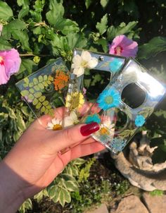 a hand holding up three pieces of glass with flowers on them