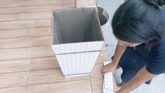 a woman standing over a box on top of a wooden floor next to a wall