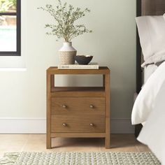 a nightstand with a potted plant on it next to a bed