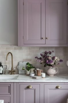 a kitchen with purple cabinets and white marble counter tops, gold faucets and vases