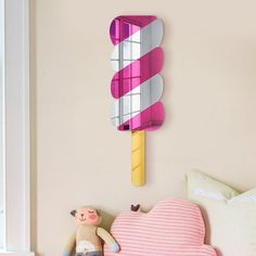 a pink and white striped ice cream lollypop clock on the wall next to a teddy bear