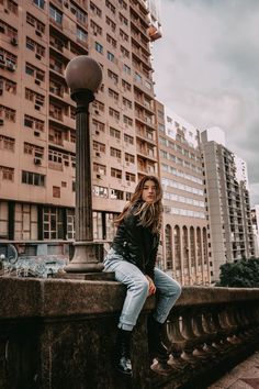 a woman is sitting on a ledge in front of a tall building and looking at the camera