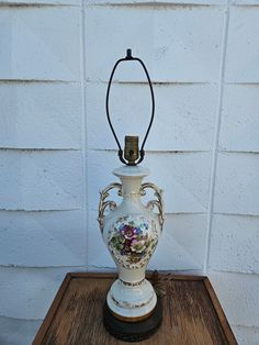 a white vase sitting on top of a wooden table next to a wall with a light