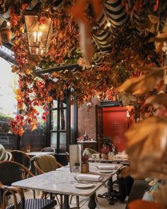 an outdoor dining area with tables and chairs covered in leaves, hanging from the ceiling