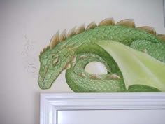 a green dragon painted on the wall next to a white framed frame with an egg in it's mouth