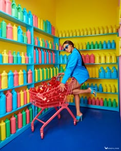 a woman pushing a shopping cart through a store filled with plastic cups and bottles on shelves