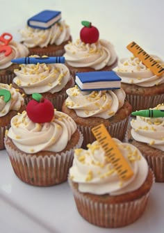 cupcakes with white frosting and school supplies on them are arranged on a plate