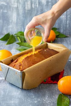 a person pouring orange juice into a loaf of bread in a box with fresh fruit around it