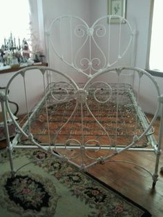 a white metal bed frame sitting on top of a wooden floor next to a rug