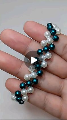 a hand holding a beaded bracelet with blue and white pearls