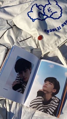 an open book sitting on top of a bed next to a white shirt and pillow