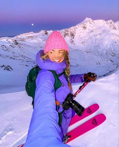 a woman sitting on top of a snow covered slope holding skis in her hand