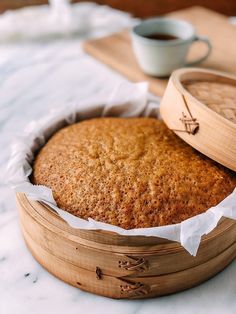 a close up of a cake in a wooden container on a table with a cup of coffee