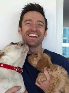 a man is holding two dogs and smiling at the camera while he holds them close to his face