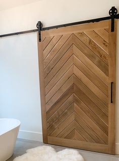 a white bath tub sitting next to a wooden sliding door in a bathroom with a rug on the floor