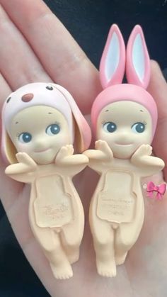 two little dolls are sitting in the palm of someone's hand, wearing bunny ears