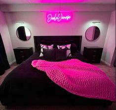 a bed with a pink blanket on top of it in a room that has black furniture