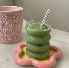 a green drink in a glass next to a pink cup with straws on it