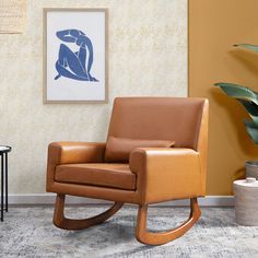 a brown leather rocking chair sitting in front of a wall with a painting on it