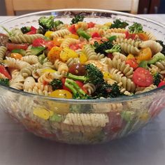 pasta salad with broccoli and tomatoes in a glass bowl on top of a table