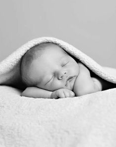 a black and white photo of a sleeping baby wrapped in a blanket with his eyes closed